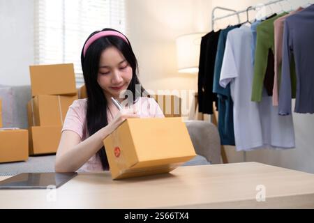 Giovane imprenditrice che confeziona gli ordini e le scatole di etichettatura per la sua attività di abbigliamento e-commerce a casa Foto Stock