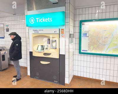 Distributore automatico di biglietti situato in una stazione ferroviaria con un passeggero in attesa nelle vicinanze Foto Stock