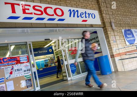 Un acquirente che ha finito di fare shopping è raffigurato uscire dall'ingresso principale di un supermercato Tesco Metro a Chippenham Wiltshire, Regno Unito. Foto Stock