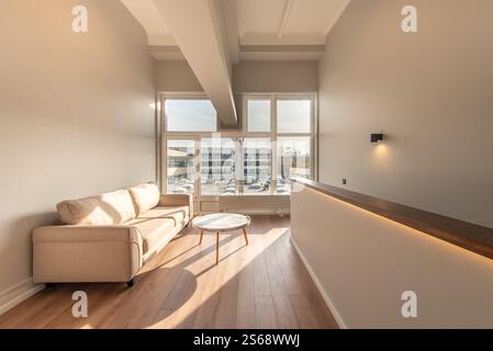 Interni luminosi ed eleganti di un'area soggiorno minimalista con un comodo divano, decor minimalista e grandi finestre che invitano alla luce naturale. Mini moderno Foto Stock