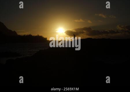 Sagoma di una figura solitaria al tramonto a Kauai, Hawaii, in piedi in cima a un terreno roccioso con il sole splendente e le spettacolari nuvole sull'Oceano Pacifico. Foto Stock