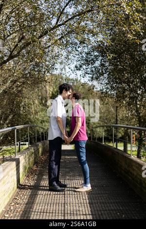 Romantica coppia gay che baciano e tengono le mani su un ponte in un parco in Brasile, celebrando l'amore e le relazioni lgbt Foto Stock