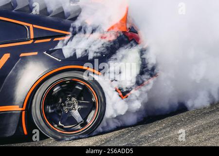 La parte posteriore di un'auto da drift su una pista ad alta velocità con fumo proveniente da pneumatici bruciati. Concorrenza Foto Stock
