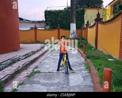 Un bambino latino di 10 anni dalla pelle scura soffre una caduta dalla bicicletta con dolore alle gambe e alle braccia Foto Stock