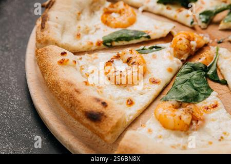 Primo piano di pizza gourmet a base di pesce con gamberi, formaggio fuso e foglie di spinaci freschi Foto Stock
