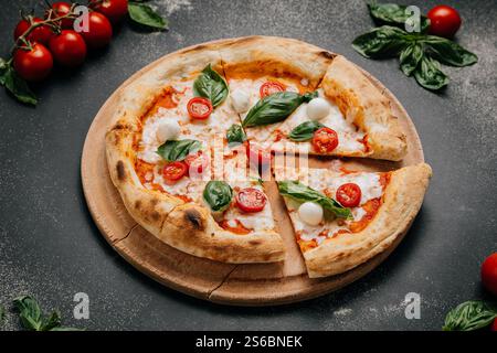 Pizza Margherita appena tagliata con basilico, mozzarella e pomodori ciliegini su un piatto rustico Foto Stock
