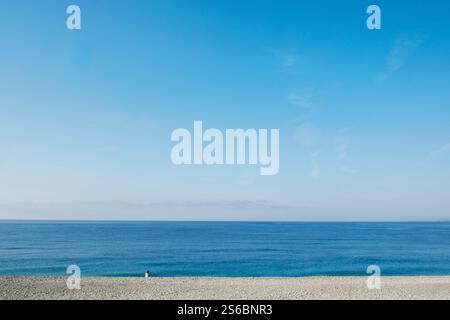 Vista posteriore di una donna solitaria seduta sulla spiaggia e affacciata sul mare Foto Stock