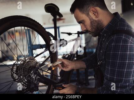 Ritratto di un bel riparatore che applica olio motore su una bicicletta in officina Foto Stock