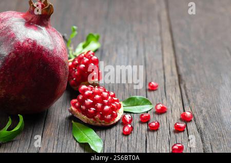 Melograno fresco maturo intero e spaccato succoso con semi e foglie su fondo rustico in legno, spazio copia concetto frutti rossi sani (Punica granatum Foto Stock
