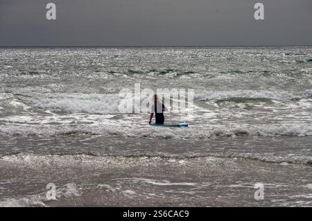 Una persona è seduta su una tavola da surf nell'oceano. L'acqua è instabile e il cielo nuvoloso Foto Stock