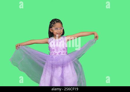La bruna latina di 5 anni con occhiali e abito da principessa è felice e divertente a giocare durante la sua vacanza Foto Stock