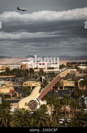 L'insegna della chitarra dell'Hard Rock Casino di Las Vegas si erge alto mentre un aereo vola attraverso nuvole spettacolari, invitando storie infinite da questa città deserta. Foto Stock