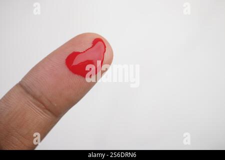 Vista ravvicinata di un dito con una goccia di liquido rossa che la attacca Foto Stock