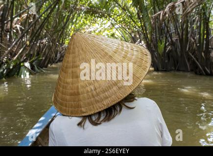Vista posteriore di una donna con tradizionale cappello conico vietnamita su una barca, Delta del Mekong, Vietnam, Asia Foto Stock
