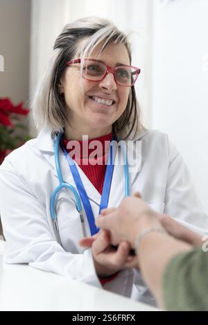 Medico donna che fornisce comfort e supporto al paziente durante una visita a casa, tenendosi per mano e mostrando empatia Foto Stock