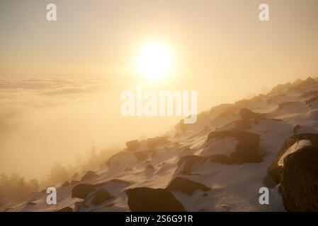 Alba sulla cima innevata della montagna. La calda luce dorata del sole che sorge bagna le nuvole in delicate sfumature di arancione e rosa. Il cielo passa dal blu intenso al pastello delicato. Foto Stock