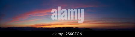 L'ipnotico tramonto dipinge il cielo con vivaci sfumature di rosa, arancione e blu. Le morbide nuvole si estendono all'orizzonte, mentre le sagome delle montagne lontane creano una scena spettacolare e tranquilla. Foto Stock