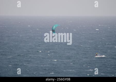 Un kiteboarder che viene tirato sull'acqua da un aquilone. Los Cristianos. Tenerife. Isole Canarie. Spagna. Foto Stock