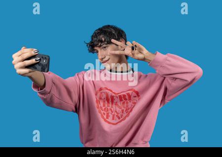 Influencer alla moda che crea contenuti per i social media, scattando un selfie e facendo il segno di pace con le dita Foto Stock