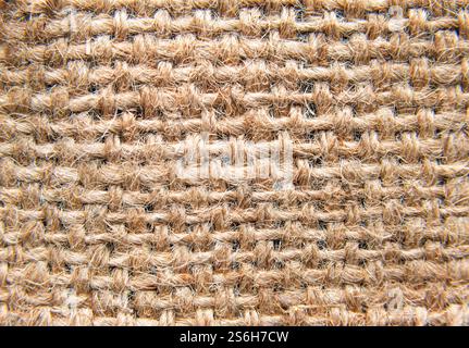 La vista ravvicinata del tessuto di iuta rivela tecniche di tessitura dettagliate e tonalità terrose, sottolineandone la consistenza naturale e la durata. Foto Stock