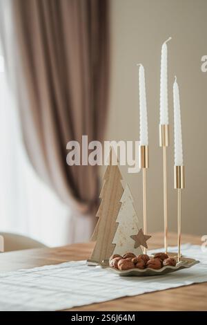 Candelabri d'oro con candele bianche, noci e spina di pesce di legno su un tavolo con tovaglia bianca, tende sullo sfondo Foto Stock