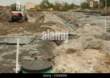 Tombini per cantieri edili, telone nero, idrante giallo, fossati mucchi di terra e escavatore. Giornata nuvolosa. Foto Stock