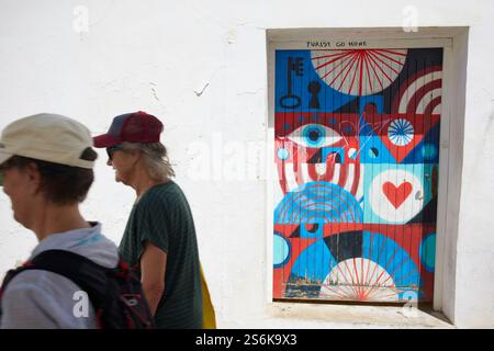 I turisti camminano davanti alla porta dipinta e i graffiti Tourist Go Home in Calle Sant Miguel, Altea, Costa Blanca, Spagna Foto Stock