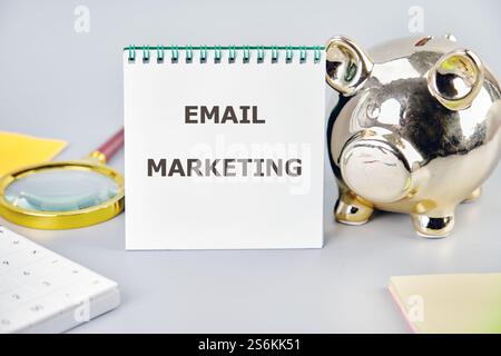 Un notebook aperto alla pagina denominata e-mail marketing si trova accanto a un salvadanaio, a una lente di ingrandimento e a un blocco note, che illustra le strategie di crescita aziendale. Foto Stock