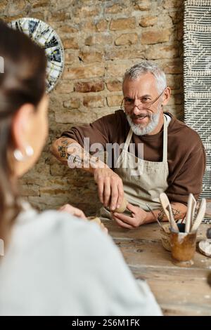 Una bella coppia matura ama modellare insieme l'argilla, condividendo il tempo di qualità in una lezione di ceramica. Foto Stock