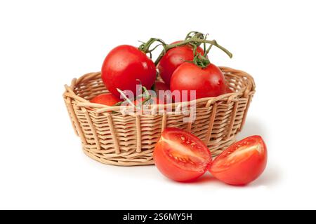 Vista sopraelevata di un cesto di vimini con pomodori di vite (lat: Solanum lycopersicum) su sfondo bianco e un frutto dimezzato davanti. Foto Stock