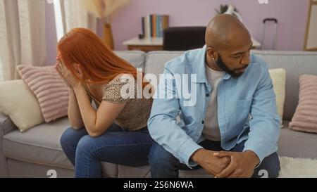 Coppia interrazziale che ha difficoltà di relazione in un salotto, con una donna che piange e un uomo che sembra preoccupato, seduto su un divano al chiuso Foto Stock