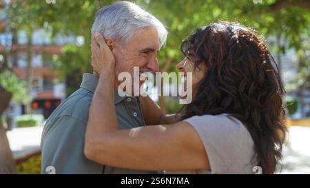 Una coppia di mezza età condivide amore e sorrisi insieme all'aperto in un parco cittadino illuminato dal sole, catturando l'essenza commovente di una splendida relazione tra di loro Foto Stock