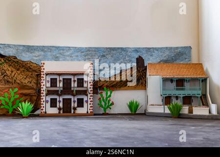 Una piccola casa è accanto a una grande casa. La piccola casa è dipinta di marrone e presenta un cactus verde sul davanti. La scena è ambientata in un deserto Foto Stock