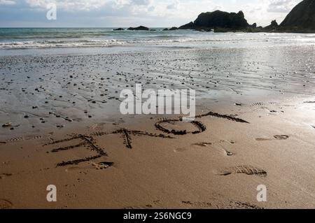 Una spiaggia con una grande roccia sullo sfondo. La sabbia è bagnata e l'acqua è calma. La parola AMORE è scritta sulla sabbia sulla spiaggia Foto Stock