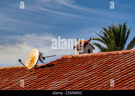 Una parabola satellitare si trova su un tetto con tegole rosse. La parabola satellitare è vecchia e arrugginita Foto Stock
