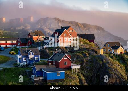 Affascinanti case dai colori vivaci sorgono sulle colline sopra Sisimiut, in Groenlandia, con la nebbia che si avvolge sullo sfondo del tramonto. Foto Stock