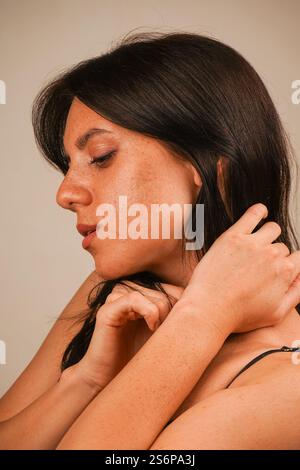 Una ragazza con i capelli neri posa in studio e non guarda la fotocamera. Vestito con un abito scuro. Tenendo le mani davanti a te e godendoti Foto Stock