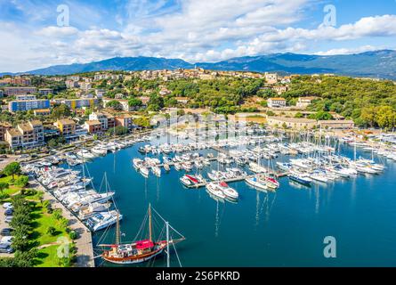 Vista aerea del porto turistico di Porto Vecchio in Corsica con yacht di lusso, barche a vela e un paesino costiero panoramico incorniciato dalle montagne e dal Mediterran Foto Stock
