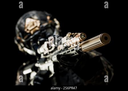 Vista focalizzata del barile equipaggiato con un soppressore tenuto da un soldato in equipaggiamento tattico. Foto Stock