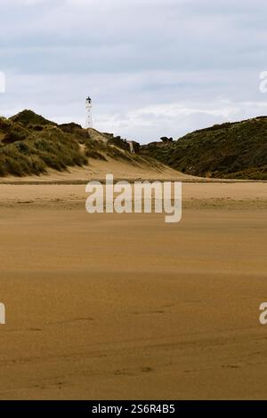 Il faro di Castlepoint sull'Isola del Nord della nuova Zelanda sorge su un'ampia spiaggia sabbiosa tra le rocce. La torre bianca è il punto di riferimento della piccola città sulla costa orientale. Foto Stock