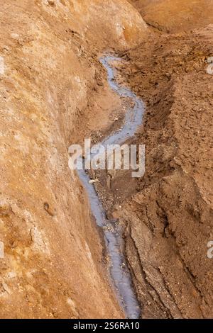 Torrente di fango grigio caldo in una fessura di suolo solforico arancione a Hverir, area geotermica di Myvatn in Islanda Foto Stock