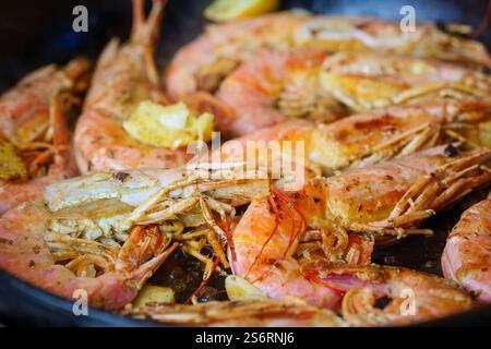 Gamberi grandi grigliati, longoustine cotti in una padella con spezie, erbe e limone su sfondo scuro. Langostino Austral su una padella nera. Foto Stock