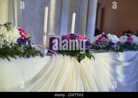 Decorazioni floreali con eleganti fiori bianchi viola, candele su tovaglie bianche drappeggiate, per creare un'atmosfera da cerimonia nuziale Foto Stock