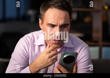 un uomo che scrive sullo smartphone di casa e rimane scioccato. uomo usa il suo smartphone rosa. Scioccate cattive notizie Foto Stock