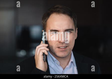 Ritratto ravvicinato di un giovane e affascinante uomo d'affari sorridente che chiama sullo smartphone. Concetto di comunicazione. primo piano della faccia di un giovane che parla al telefono Foto Stock