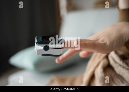 La donna utilizza il pulsossimetro al dito per misurare il livello di ossigeno nel sangue. Il dispositivo elettronico con monitor mostra la saturazione dell'ossigeno e la frequenza del polso, garantendo la massima sicurezza Foto Stock