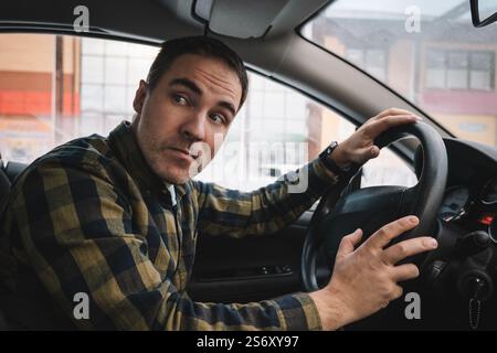 Un uomo guarda con stupore da dietro il volante dell'auto verso il retro dell'auto. vista laterale. Foto Stock