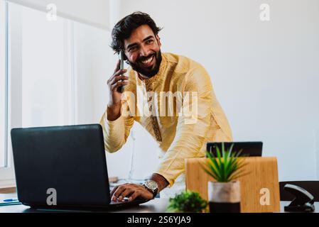 Un uomo d'affari pakistano in ufficio. Giovane uomo d'affari con abiti tradizionali che lavora nel suo ufficio. Venditore che effettua una telefonata con i clienti Foto Stock
