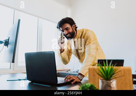 Un uomo d'affari pakistano in ufficio. Giovane uomo d'affari con abiti tradizionali che lavora nel suo ufficio. Venditore che effettua una telefonata con i clienti Foto Stock