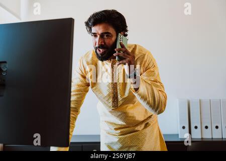 Un uomo d'affari pakistano in ufficio. Giovane uomo d'affari con abiti tradizionali che lavora nel suo ufficio. Venditore che effettua una telefonata con i clienti Foto Stock